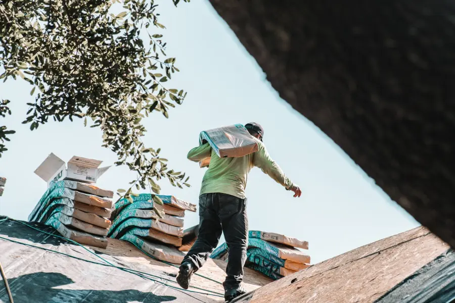 Roofer carrying a bundle of shingles up a roof